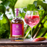 Bottle of Highgrove Rhubarb Pink Gin with a glass of pink cocktail on a wooden surface with rhubarb in the background.