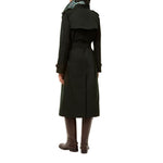 A person shown from the back wearing a long dark green trench coat with a belt, brown knee-high boots, and a green plaid neck gaiter, against a plain white background.