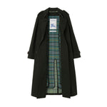 A long dark green trench coat with a green and blue plaid lining, displayed flat against a solid white background. A white Burberry brand tag is visible inside the collar.
