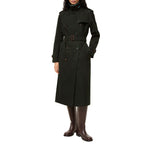 A model wearing a dark green double-breasted trench coat with a matching belt, paired with dark brown leather boots, against a solid white background.