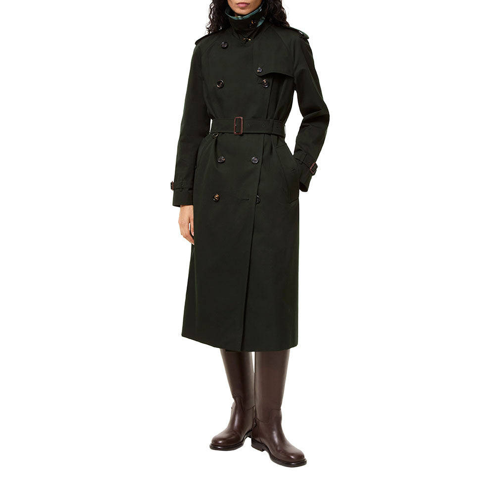 A model wearing a dark green double-breasted trench coat with a matching belt, paired with dark brown leather boots, against a solid white background.