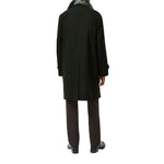 A person shown from the back wearing a long dark green coat, dark trousers, and black shoes against a plain white studio background.