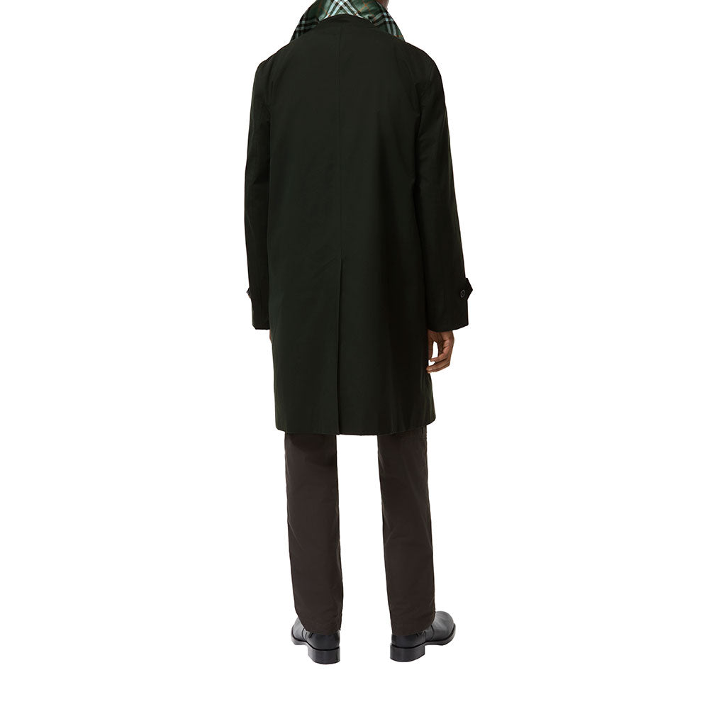 A person shown from the back wearing a long dark green coat, dark trousers, and black shoes against a plain white studio background.