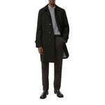 A model wearing a dark green mid-length overcoat over a gray sweater, dark brown trousers, and black leather shoes, shot against a solid white background.