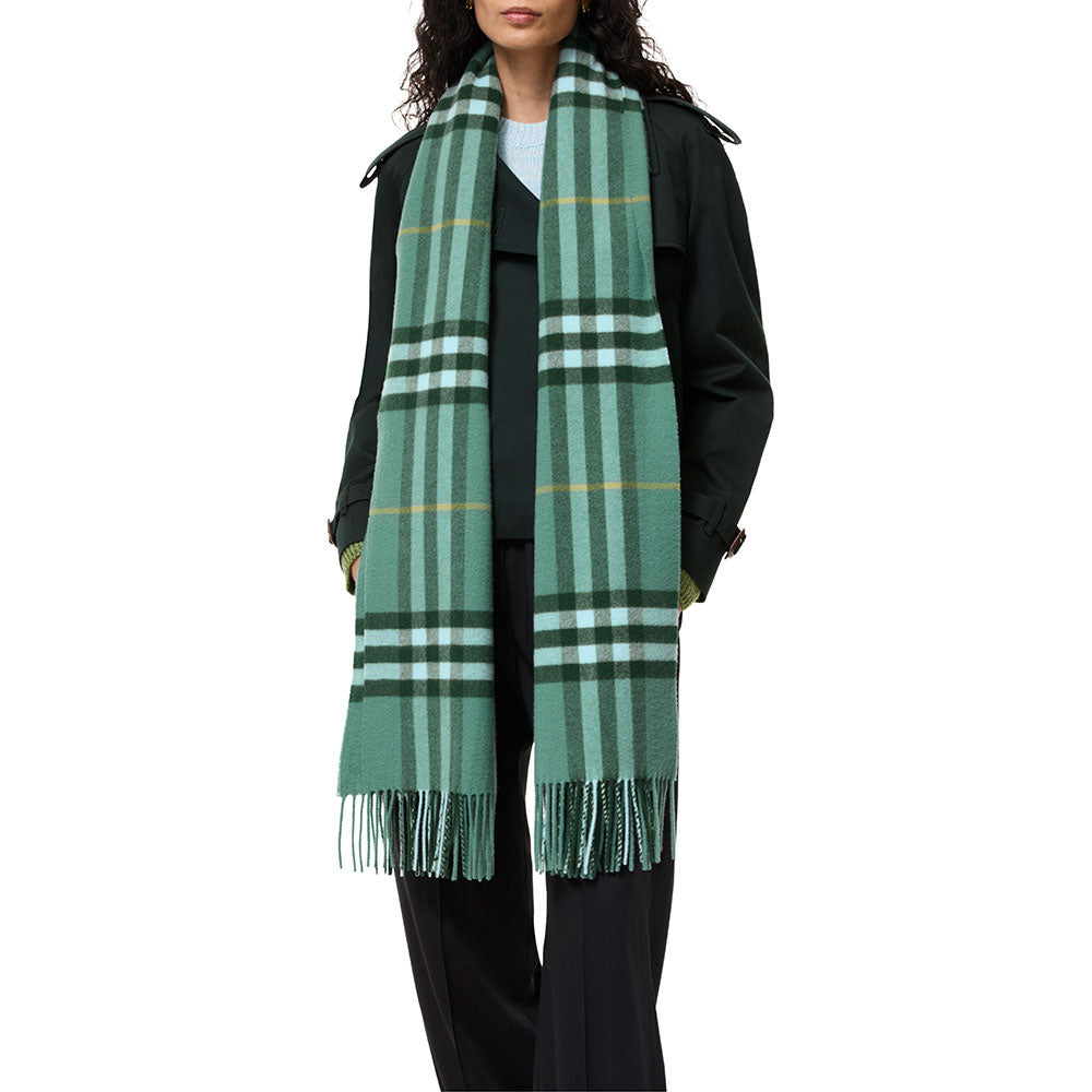 A model wearing a classic green plaid scarf with white and yellow stripes, styled over a dark green trench coat against a plain white background.