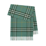 A green plaid scarf with fringe at the bottom, featuring intersecting stripes of dark green, light gray, and thin yellow lines, shown flat against a white background.