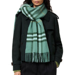 A model wearing a classic green plaid scarf with white and yellow stripes, styled over a dark green trench coat against a plain white background.