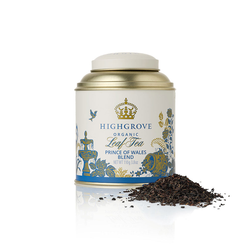 Highgrove Organic Leaf Tea canister in a white and gold tin with blue and gold illustrations, shown with a small pile of loose dark tea leaves in front on a white background.
