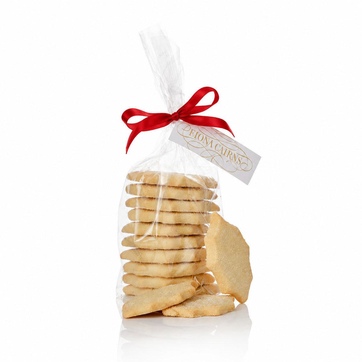 A clear cellophane bag filled with assorted sugar holly-shaped shortbread biscuits, tied with a red ribbon and a white tag reading 'Fiona Cairns', on a white background.