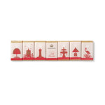 Six individually wrapped milk chocolate bars arranged in a row on a plain white background. The wrappers are cream-colored with red silhouettes of coastal landmarks and the brand name 'MILK CHOCOLATE' is visible on the centre wrapper.
