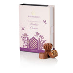 Highgrove Praline Crowns chocolate box packaging in pale pink with purple floral illustrations, shown with three chocolate pieces in front on a white background.