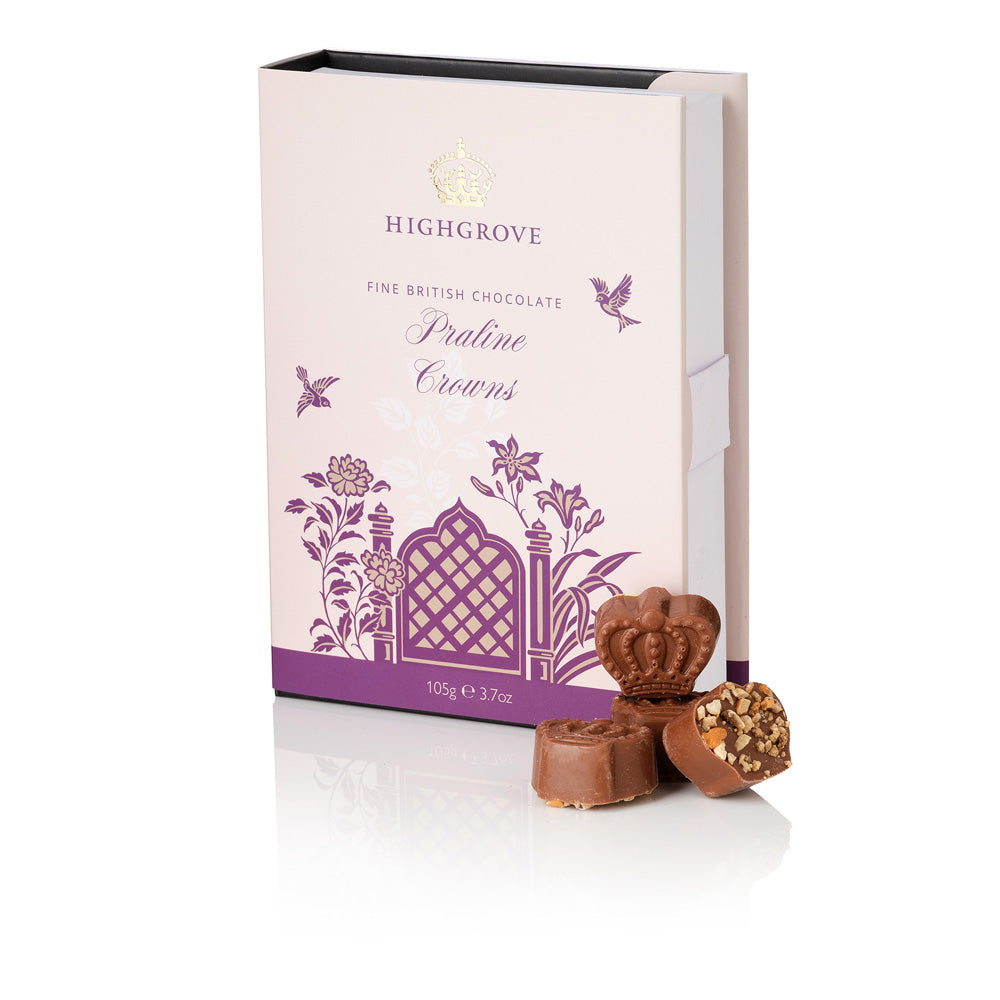Highgrove Praline Crowns chocolate box packaging in pale pink with purple floral illustrations, shown with three chocolate pieces in front on a white background.