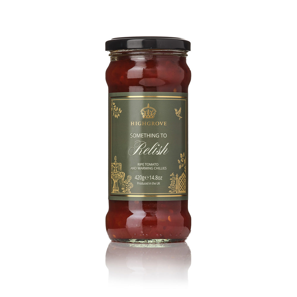 A glass jar of Highgrove Something to Relish spise tomato and warming chilies, featuring a dark olive green label with gold lettering and a black lid, set against a clean white background with a soft reflection.