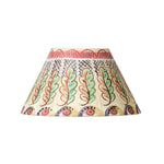 A conical fabric lampshade featuring a hand-painted folk art pattern with stylized leaves and geometric motifs in green, red, blue, and yellow on a cream background.