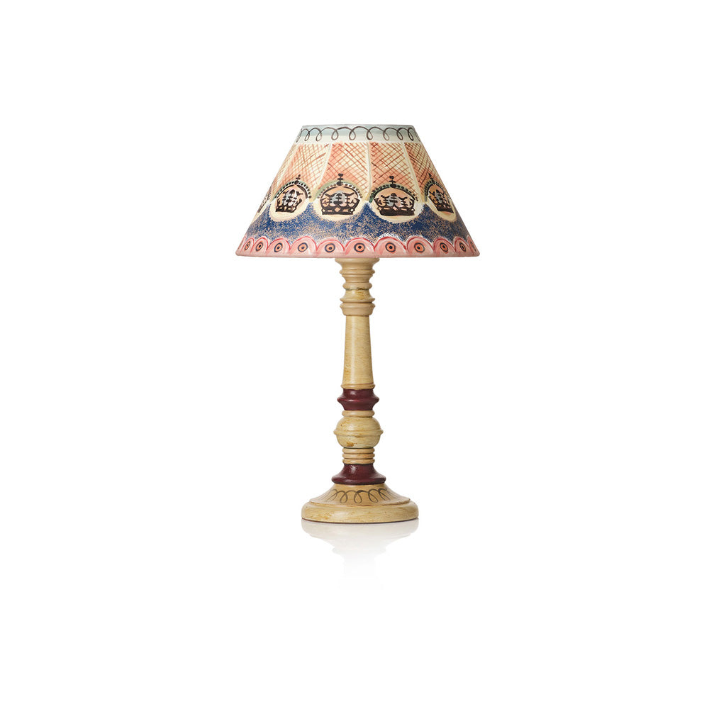 A vintage-style table lamp with a patterned fabric shade featuring crown motifs in blue, orange, and beige, supported by a turned wooden stem with dark reddish-brown accents and a round base, shown on a white background.