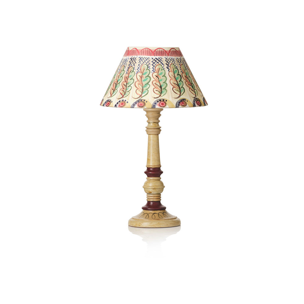 A traditional table lamp with a carved wooden base and a patterned fabric shade featuring green, red, and blue motifs on a cream background, set against a plain white background.