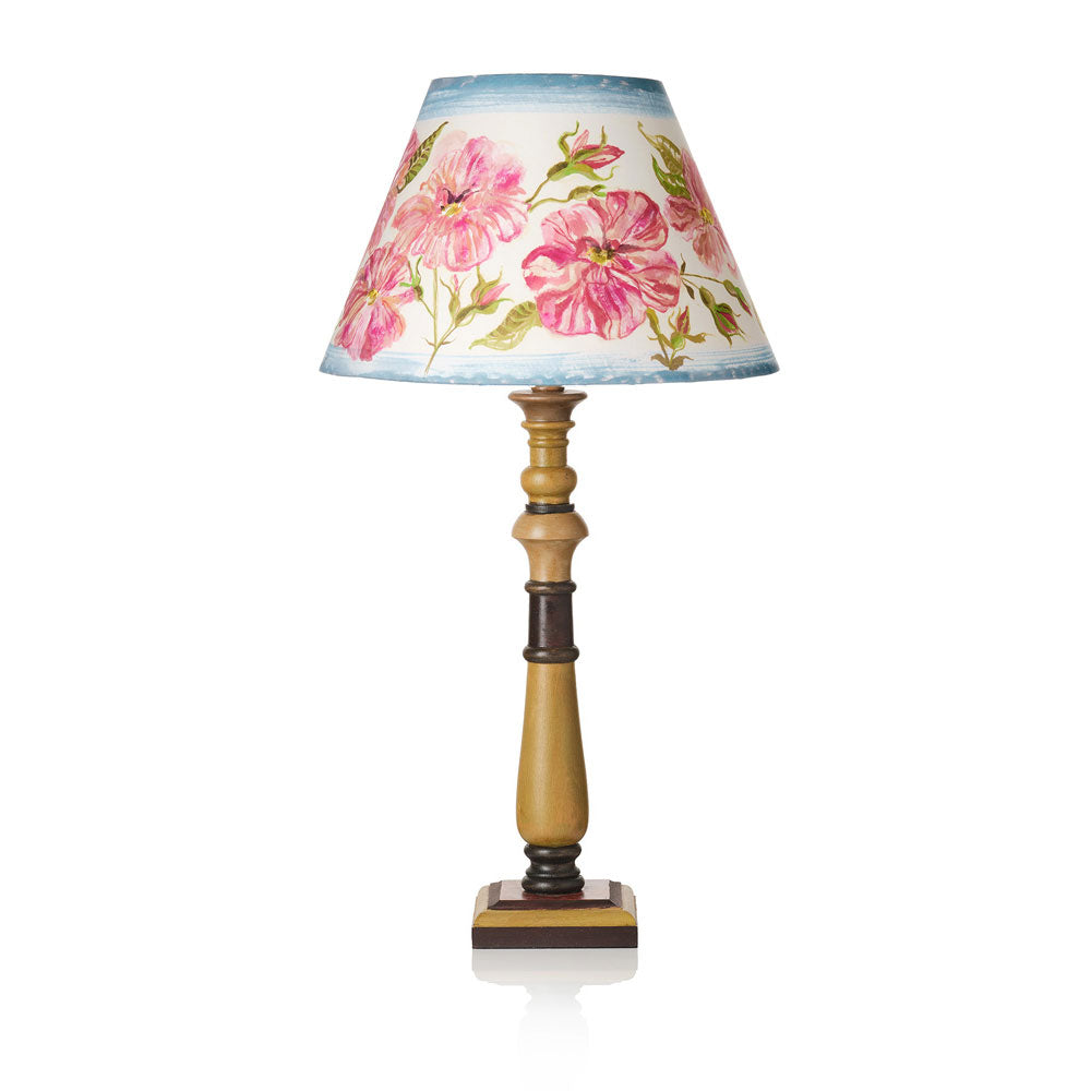 A table lamp with a conical shade featuring a pink hibiscus floral pattern on a light blue and white background, mounted on a turned wood base with a square dark brown footed pedestal.