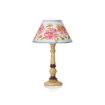 A vintage-style table lamp with a cream-colored turned wood pedestal base and a conical fabric shade decorated with a pink floral pattern on a light blue background.