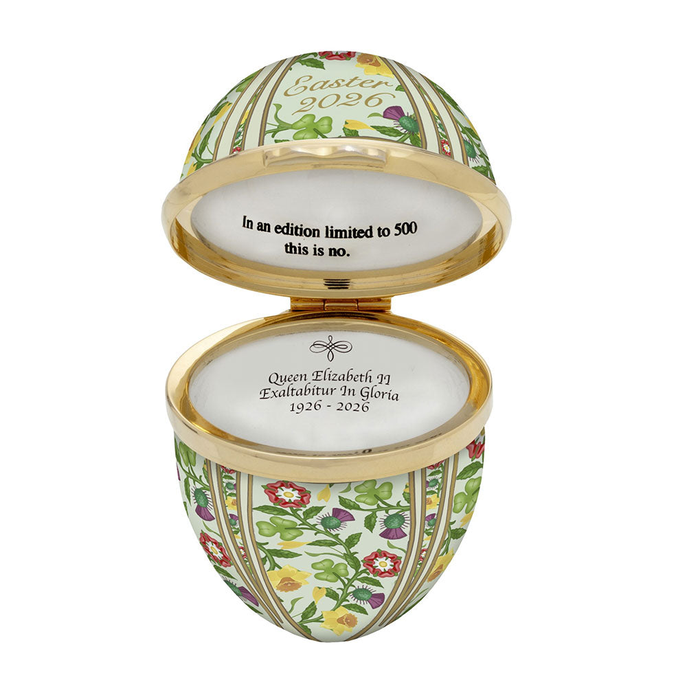 Decorative egg-shaped enamel box with floral patterns and text on a white background