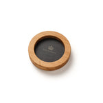 A circular wooden coasters set on a white background, featuring a light natural wood outer ring and a slate backing with the Highgrove brand name and crown logo printed in gold.