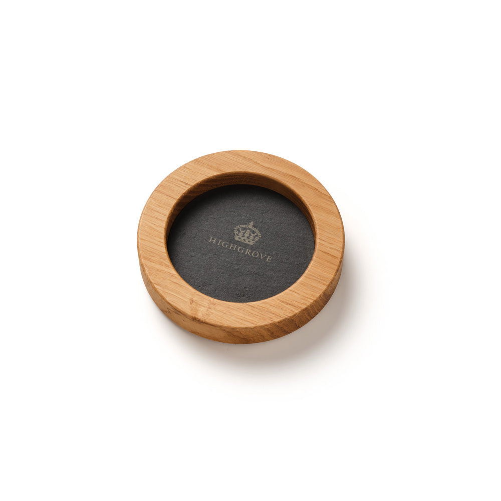 A circular wooden coasters set on a white background, featuring a light natural wood outer ring and a slate backing with the Highgrove brand name and crown logo printed in gold.
