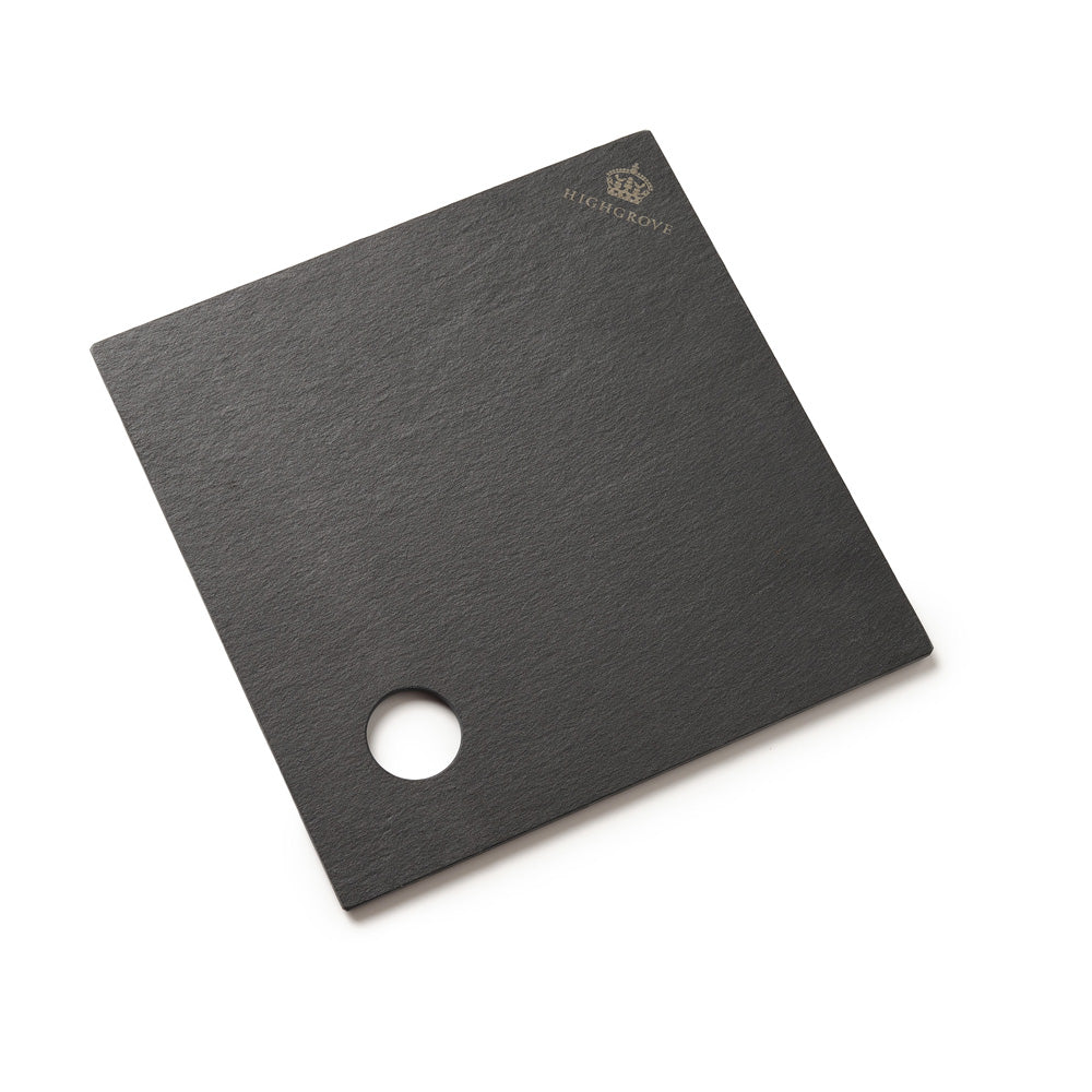 A square black slate serving board with a circular cutout near one corner and a small gold crown logo with the brand name 'HIGHGROVE' printed in the top right, shown on a clean white background.