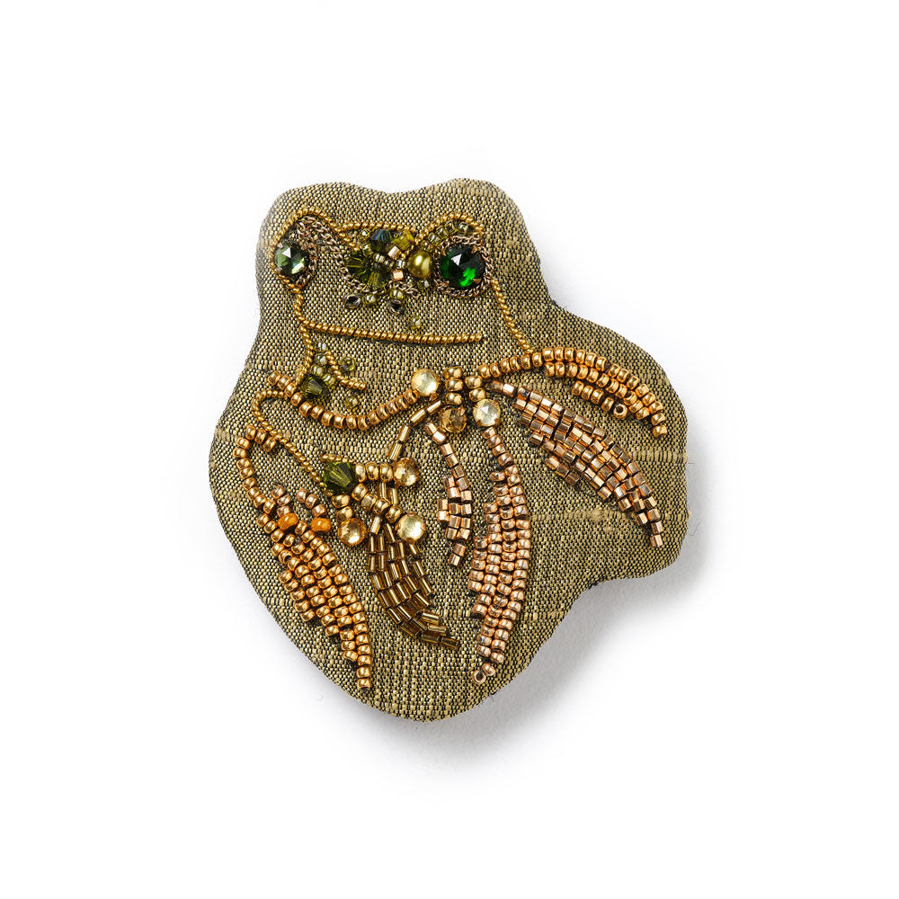 Decorative frog brooch with beads and gemstones on a beige background
