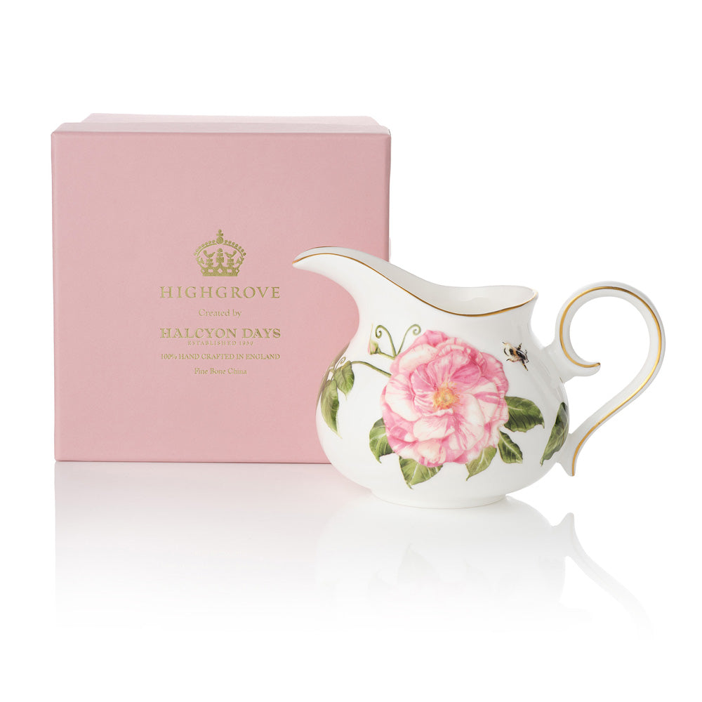 White ceramic creamer jug with The King's Rose floral design and gold accents, next to a pink box with gold 'Highgrove' writing on a white background.