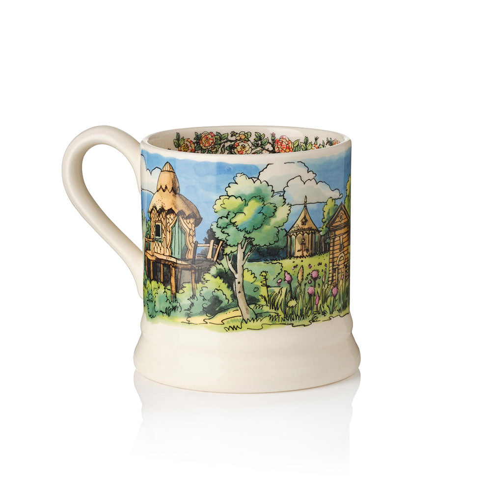 An off-white ceramic mug featuring a hand-painted illustration of the Treehouse in the Stumpery at Highgrove, the Dovectore, trees, flowers, beehive and a blue sky.